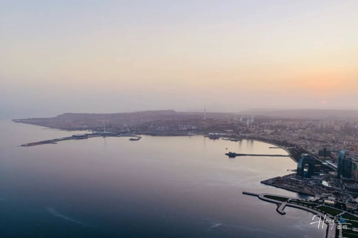 A coastal city seen across calm water at sunrise, photographed by Heng Lu